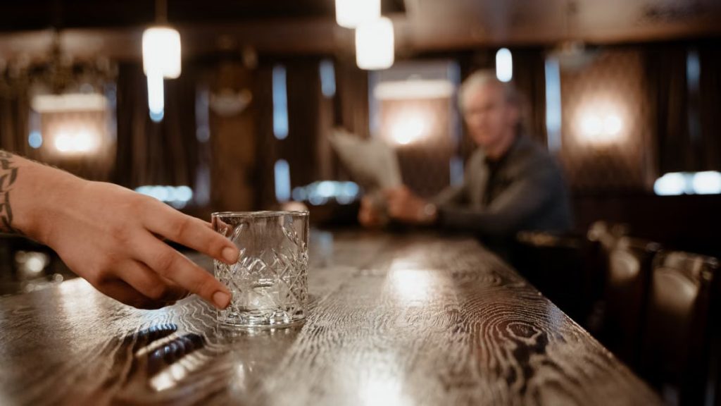 A warm bar setting with a close-up of a hand holding a crystal glass. Blurred background.