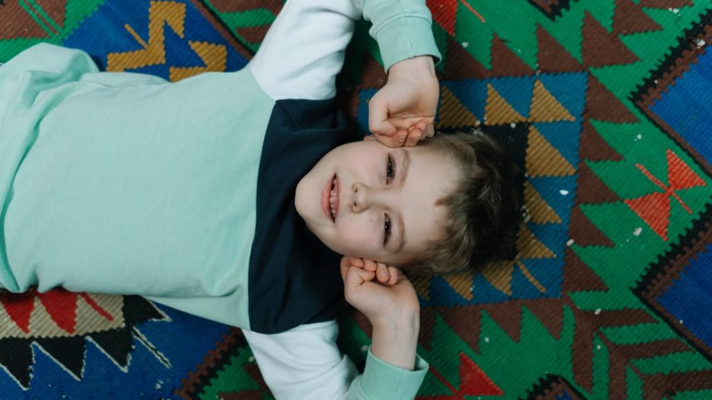 A happy child lying on a vibrant geometric-patterned carpet, smiling and relaxed.